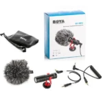Boya BY-MM1 Universal Cardioid Microphone complete kit, including the compact shotgun microphone with red shock mount, furry windscreen muff, coiled 3.5mm audio cable with splitter adapter, and a black BOYA drawstring carrying pouch — shown alongside its retail packaging box.