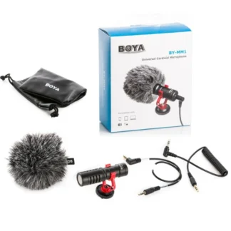 Boya BY-MM1 Universal Cardioid Microphone complete kit, including the compact shotgun microphone with red shock mount, furry windscreen muff, coiled 3.5mm audio cable with splitter adapter, and a black BOYA drawstring carrying pouch — shown alongside its retail packaging box.